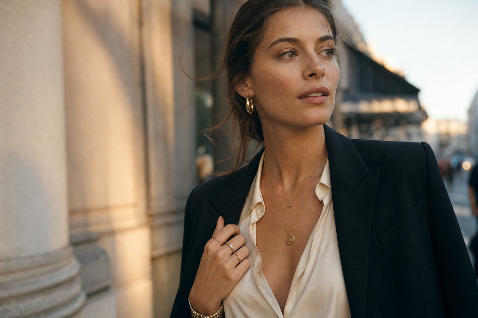 Woman styling layered gold jewelry with a cream blouse and black blazer