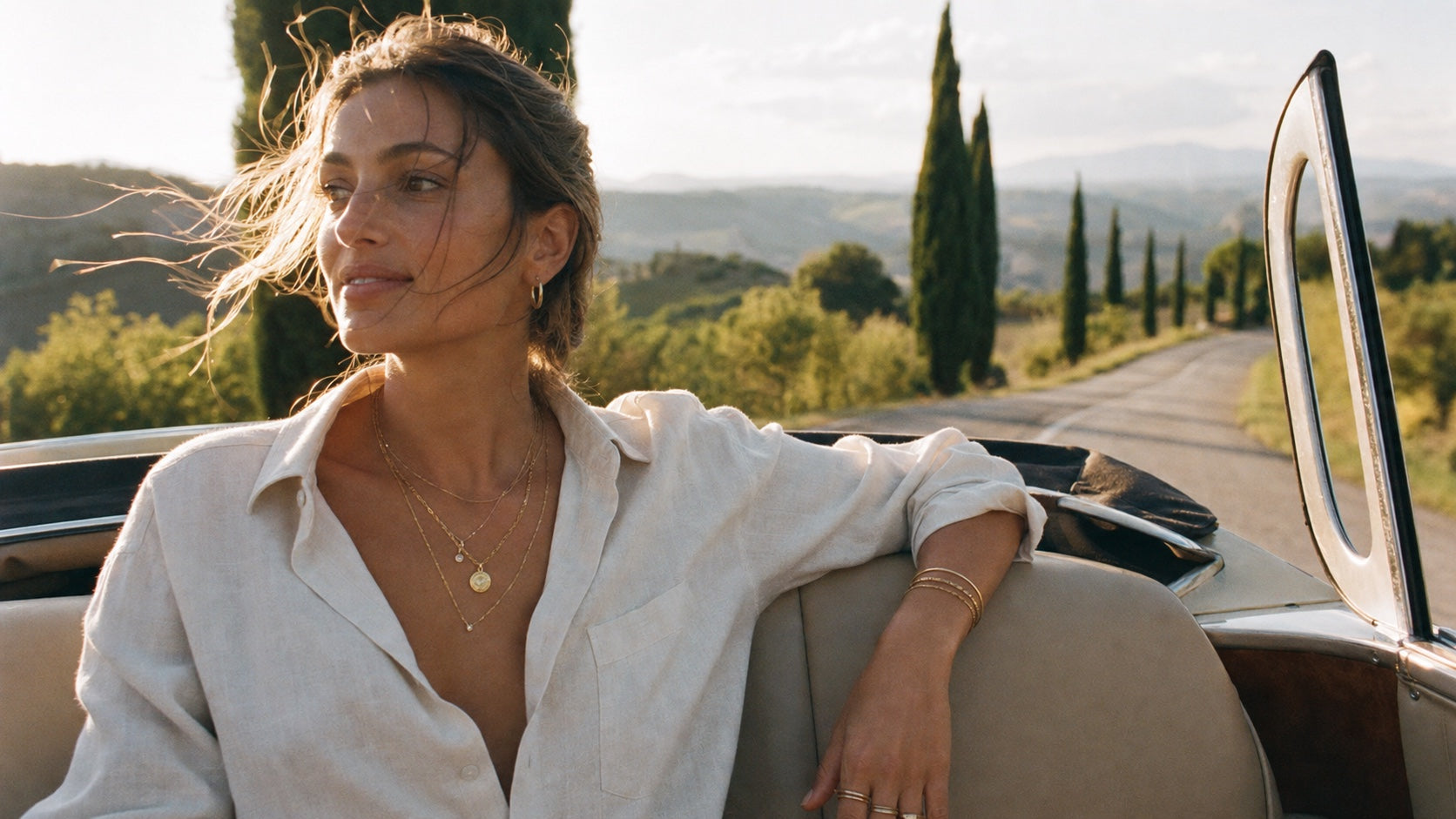 Model wearing layered Suri solid gold jewelry in a vintage convertible in Tuscany