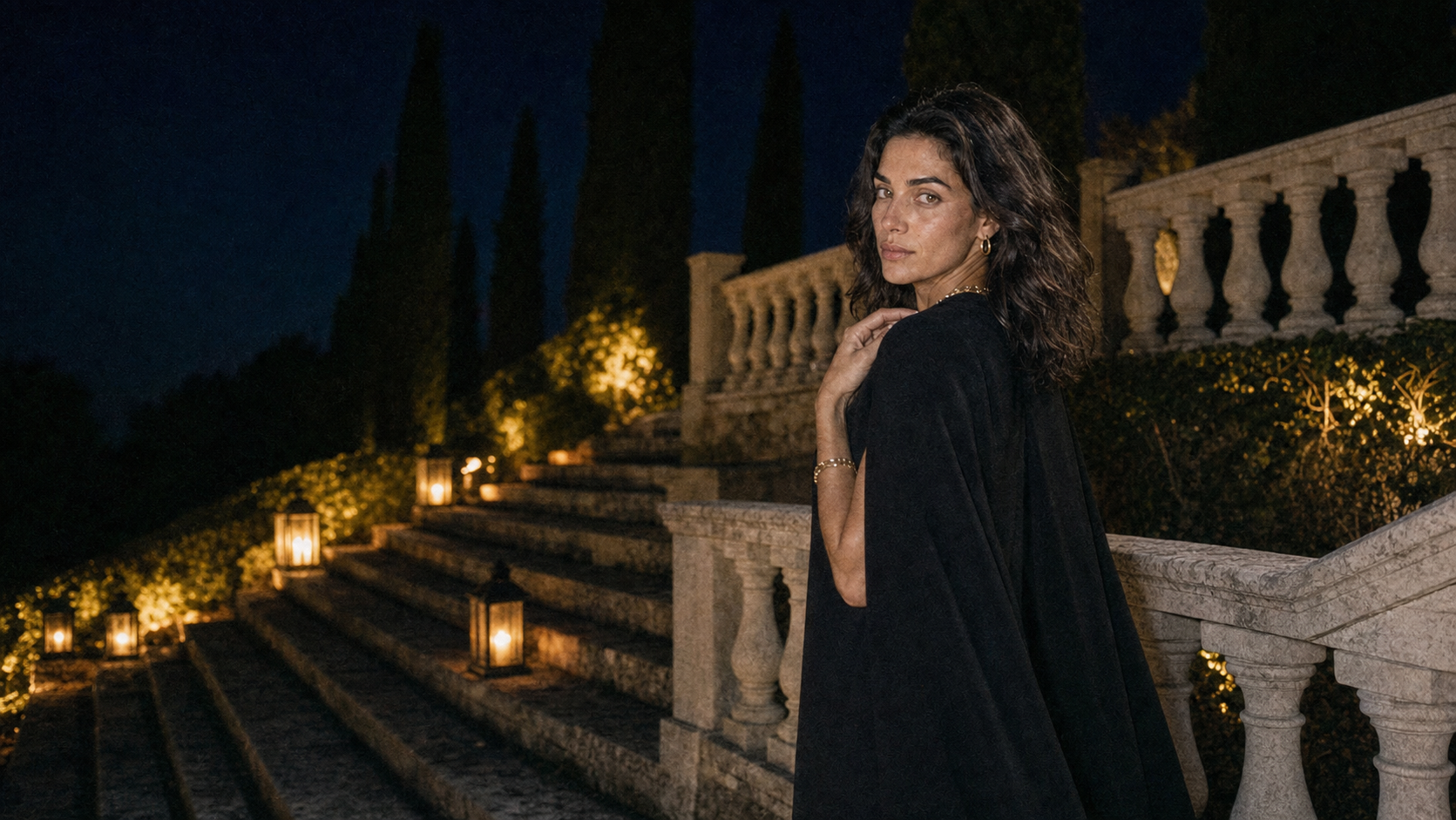 Suri model wearing layered jewelry in a lantern-lit night garden